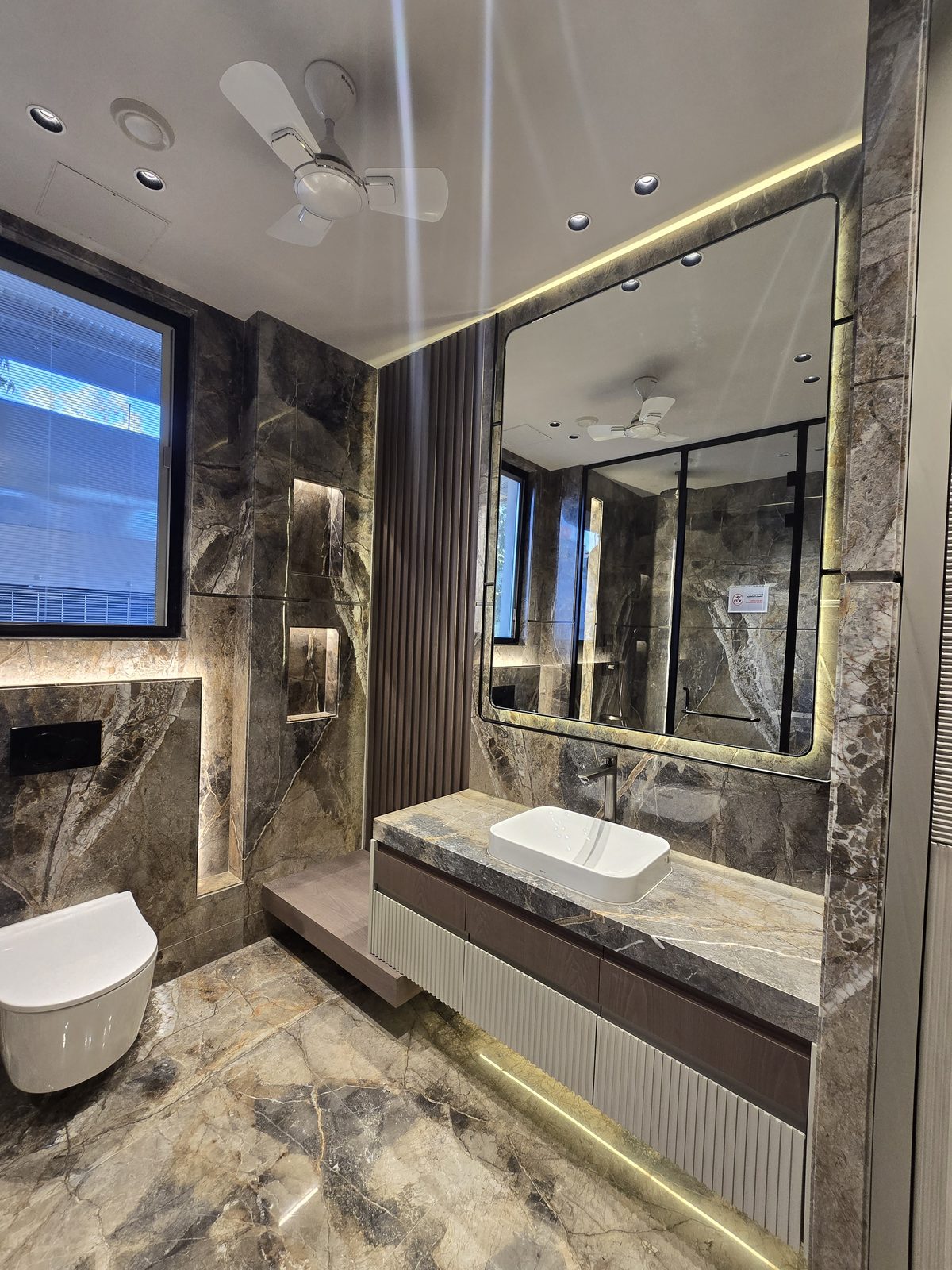 Bathroom in an Ekum Homes builder floor in South Delhi clad in brown marble with a floating vanity and backlit mirror