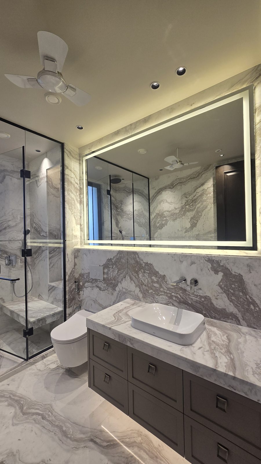 Bathroom with a glass walk-in shower and book-matched veined marble in an Ekum Homes South Delhi builder floor
