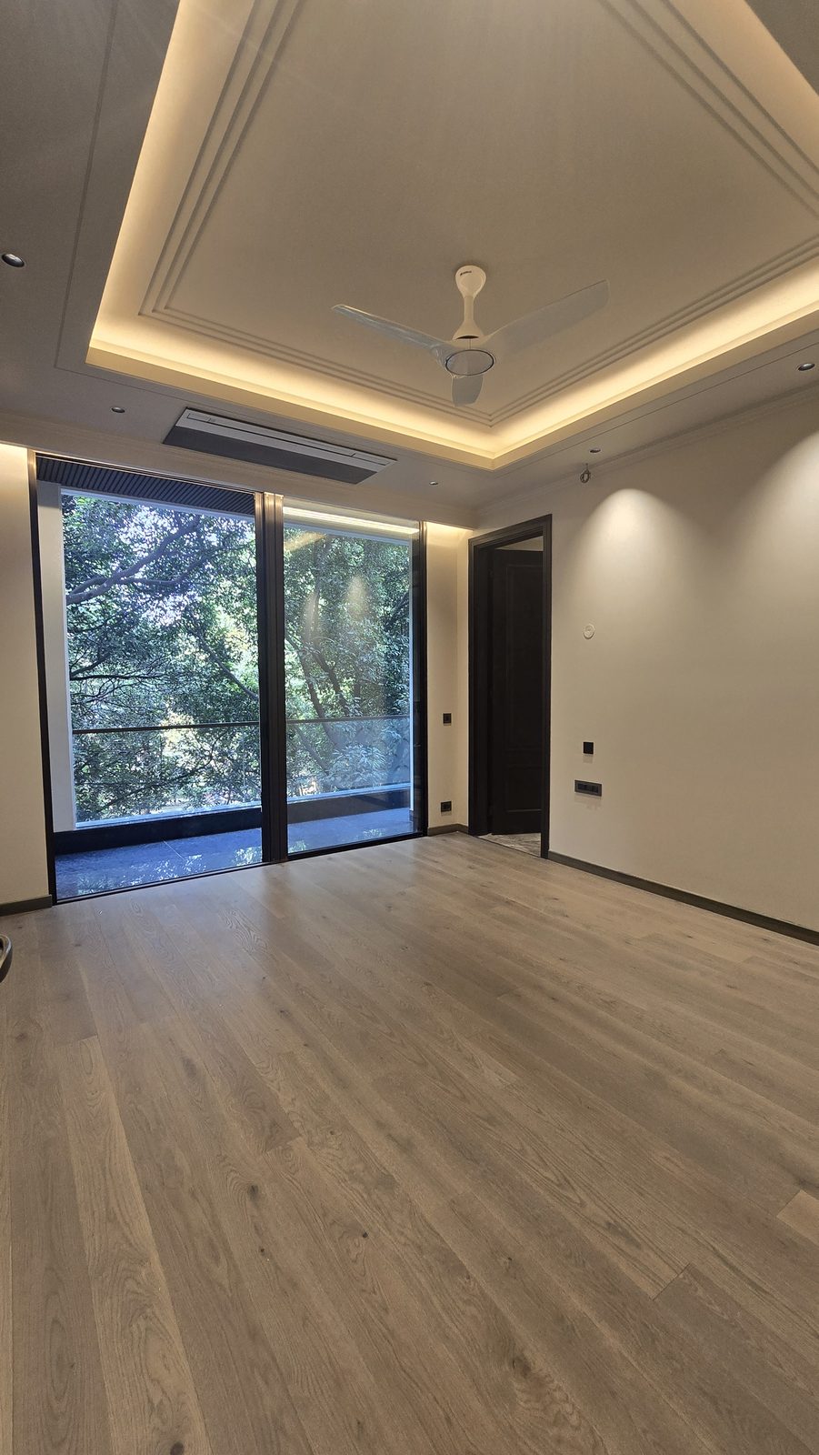Bedroom with engineered wood flooring and full-height balcony glazing in an Ekum Homes builder floor in South Delhi