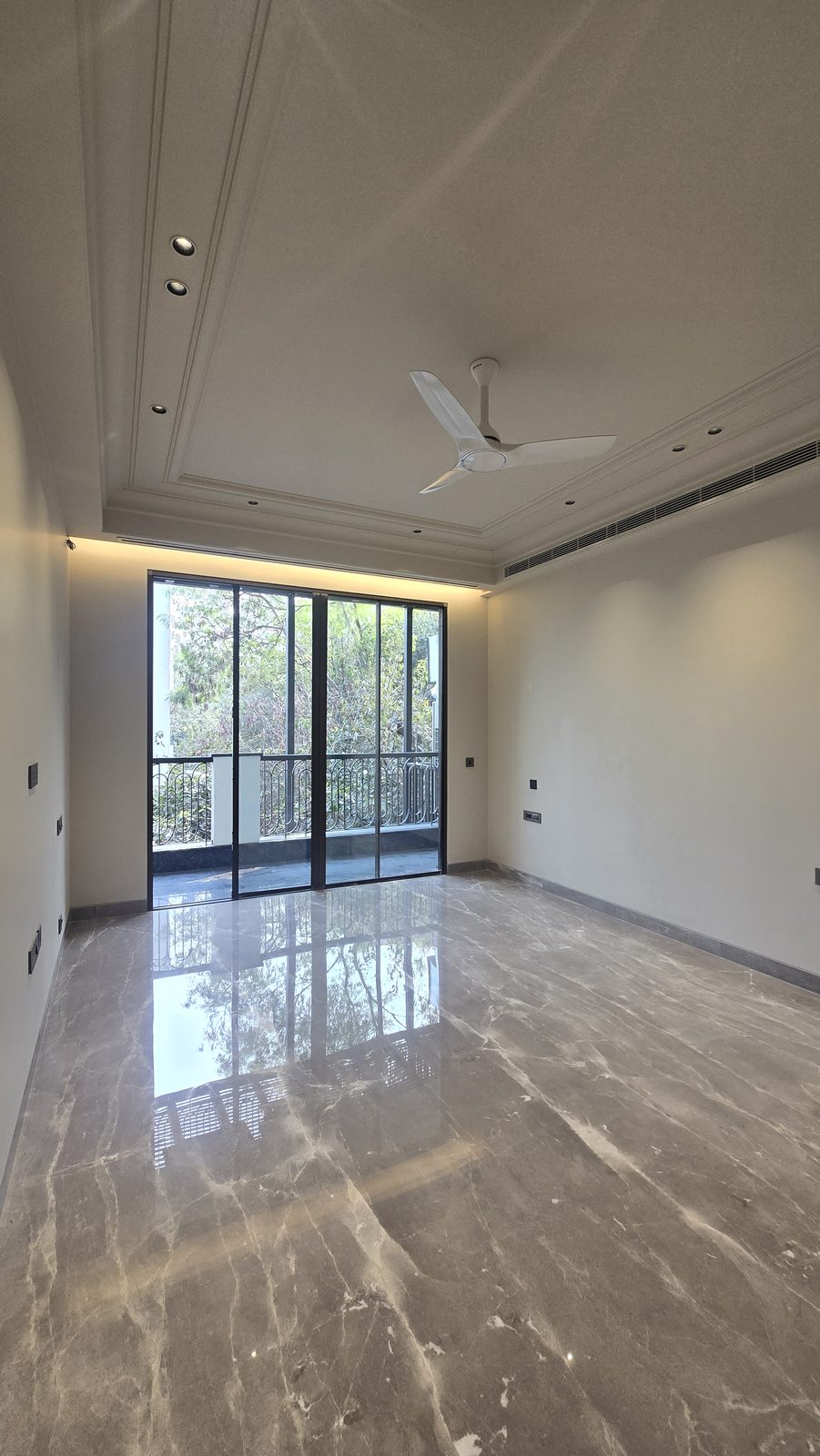 Bedroom in an Ekum Homes builder floor in South Delhi with marble flooring, a coffered cove-lit ceiling and balcony access
