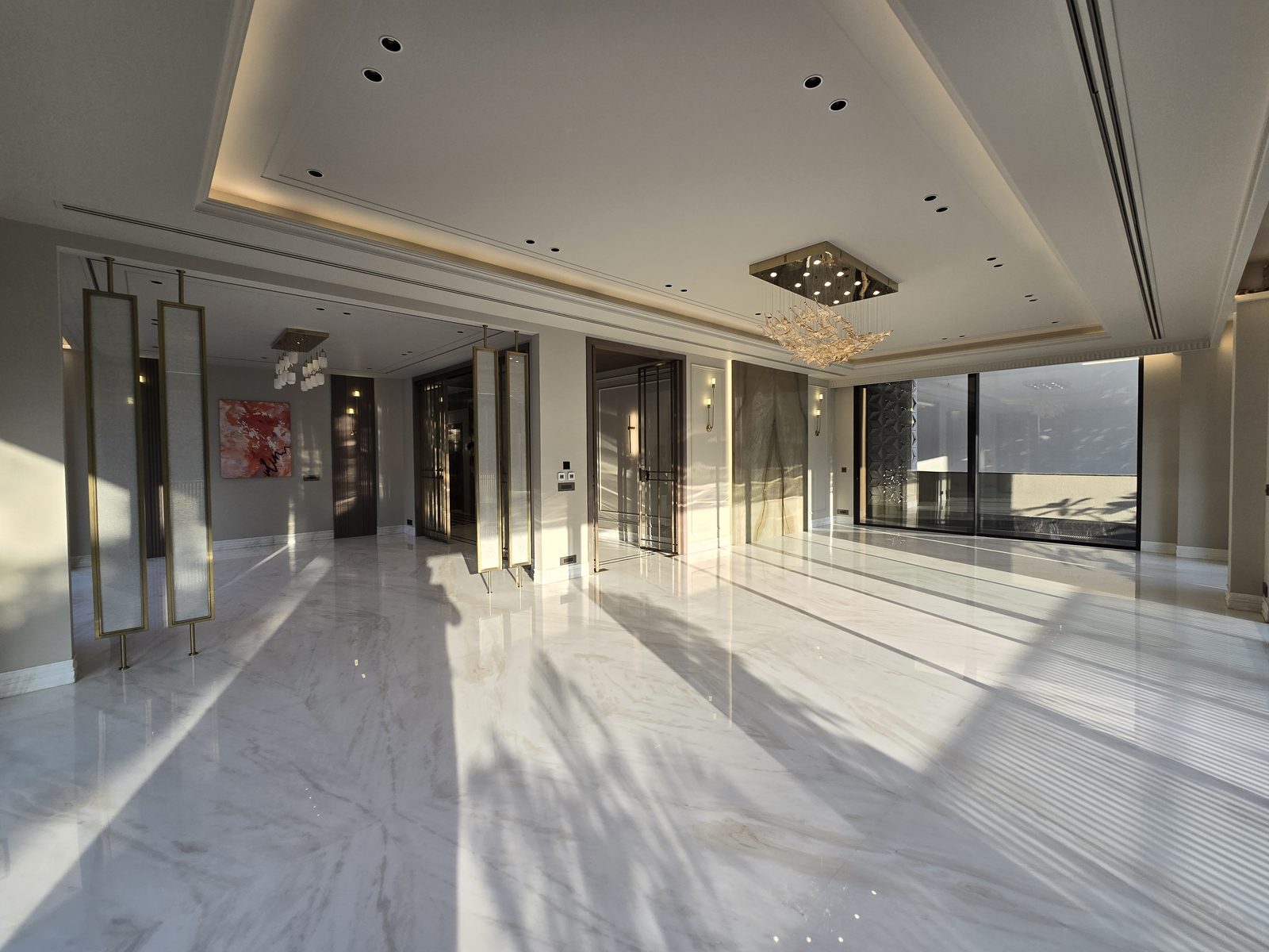 Drawing room of an Ekum Homes builder floor in South Delhi with white marble flooring, layered chandeliers and full-height glazing