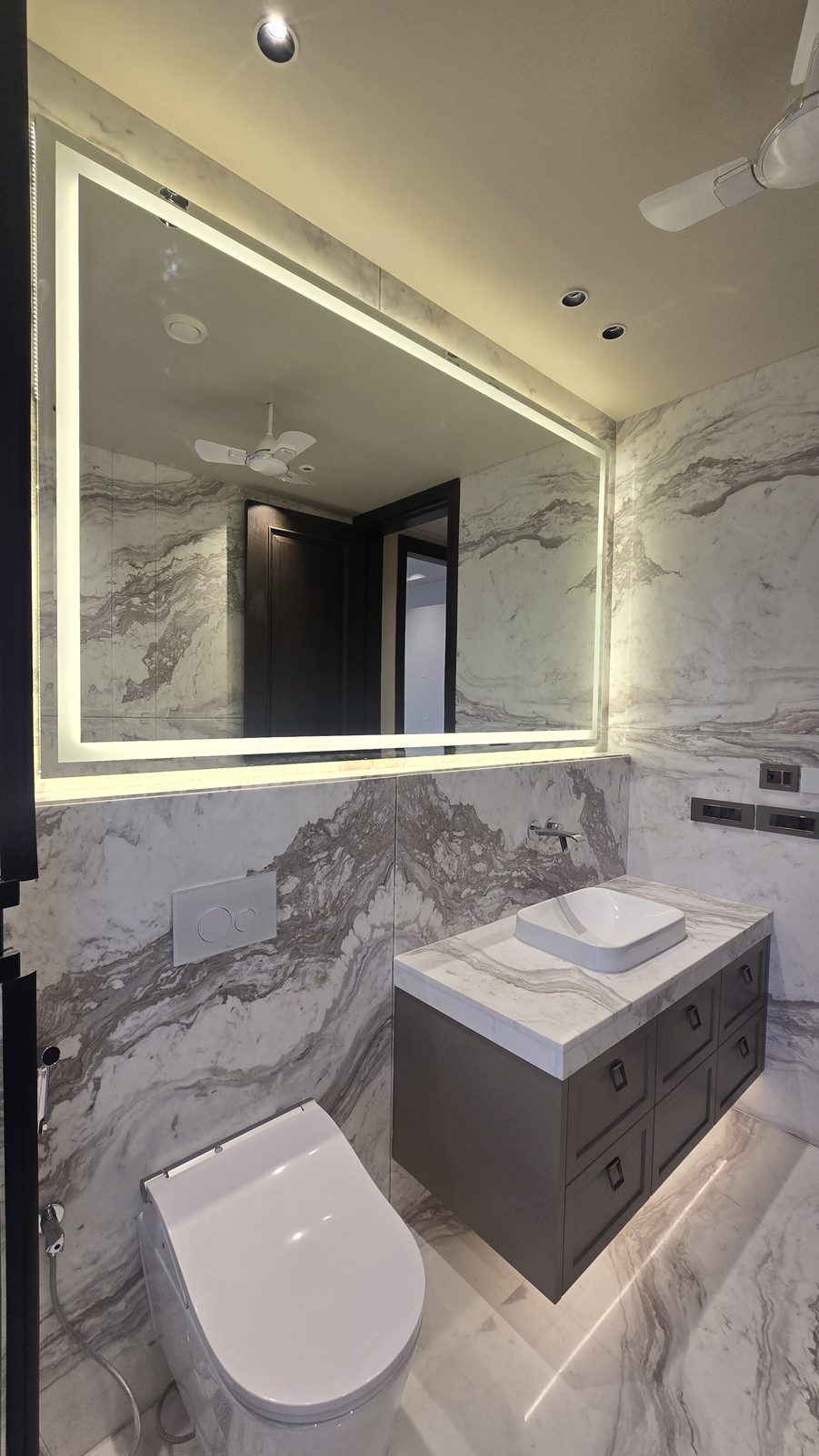 Guest bathroom with a backlit mirror and book-matched veined marble in an Ekum Homes builder floor in South Delhi