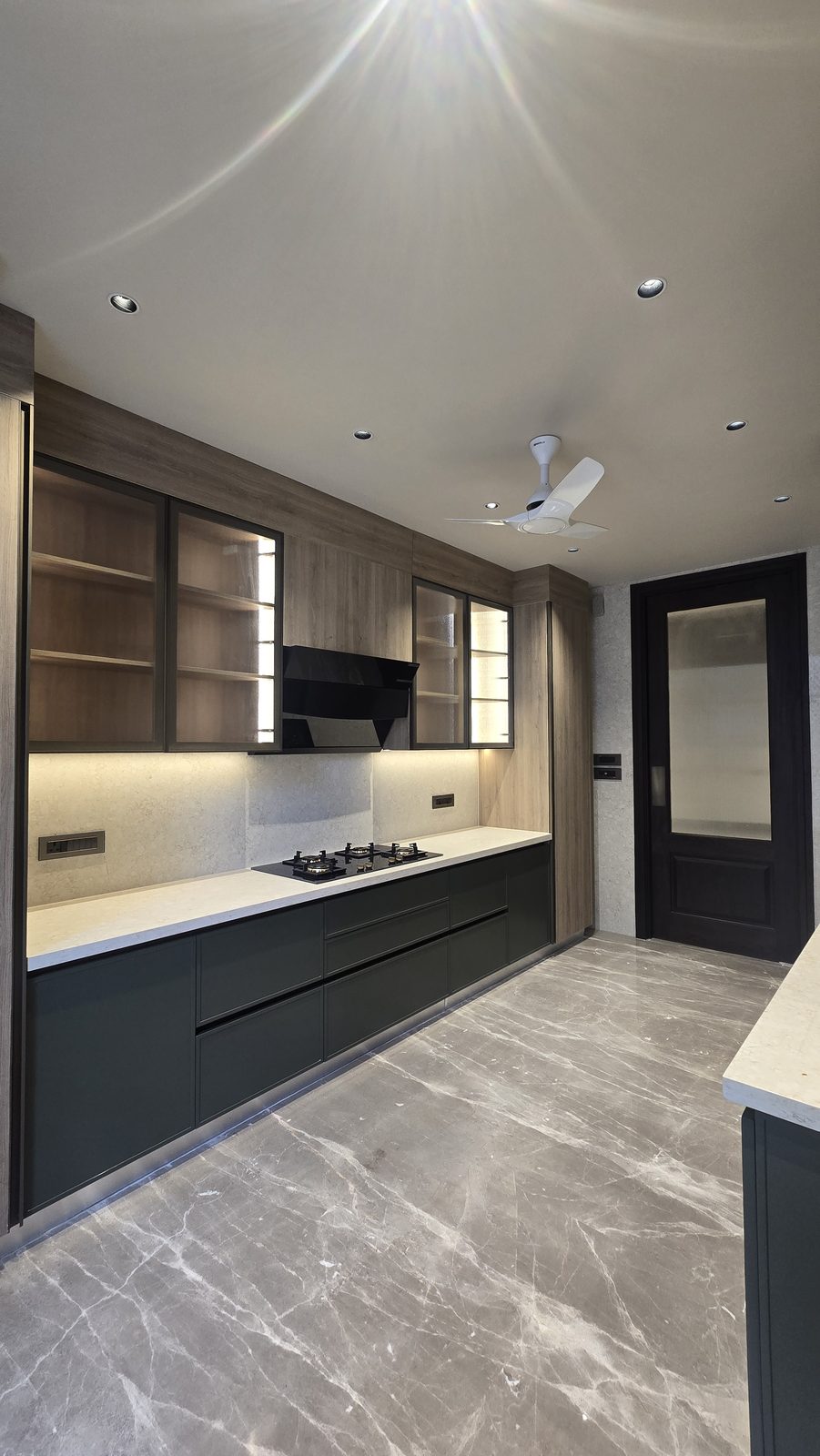 Kitchen with charcoal cabinetry, glass-front upper units and grey marble flooring in an Ekum Homes South Delhi builder floor
