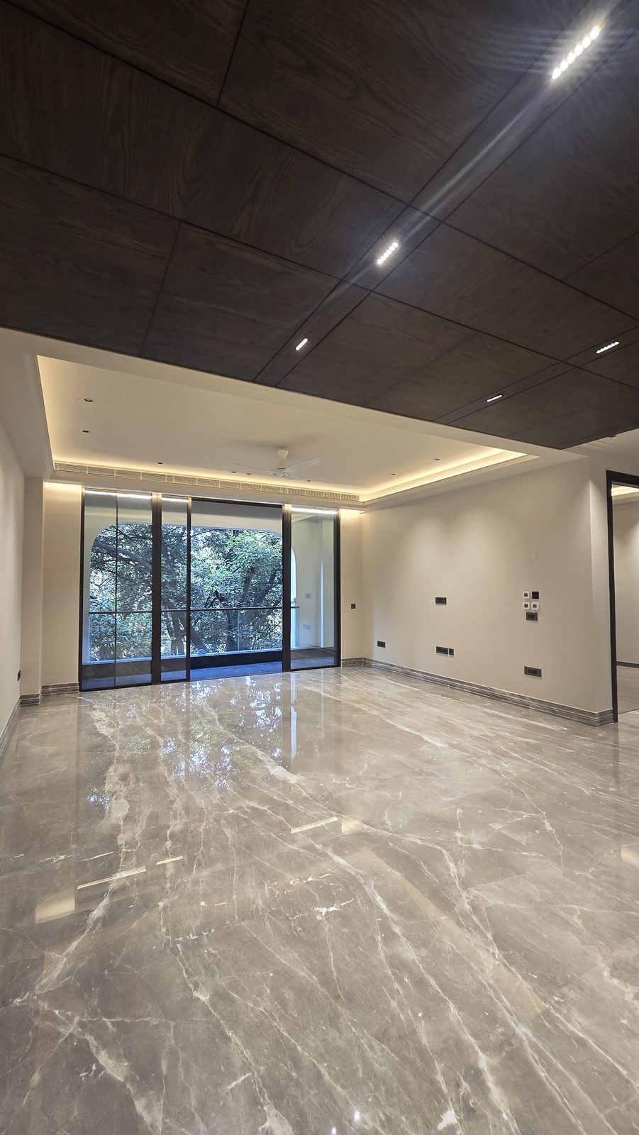 Ekum Homes living room in South Delhi with arched sliding glazing opening to a mature tree canopy