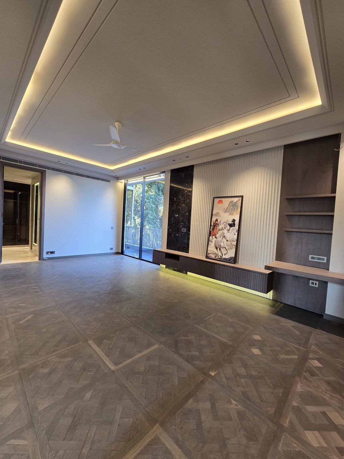 Living room of an Ekum Homes South Delhi builder floor with parquet-pattern stone flooring, cove-lit ceiling and fluted media wall