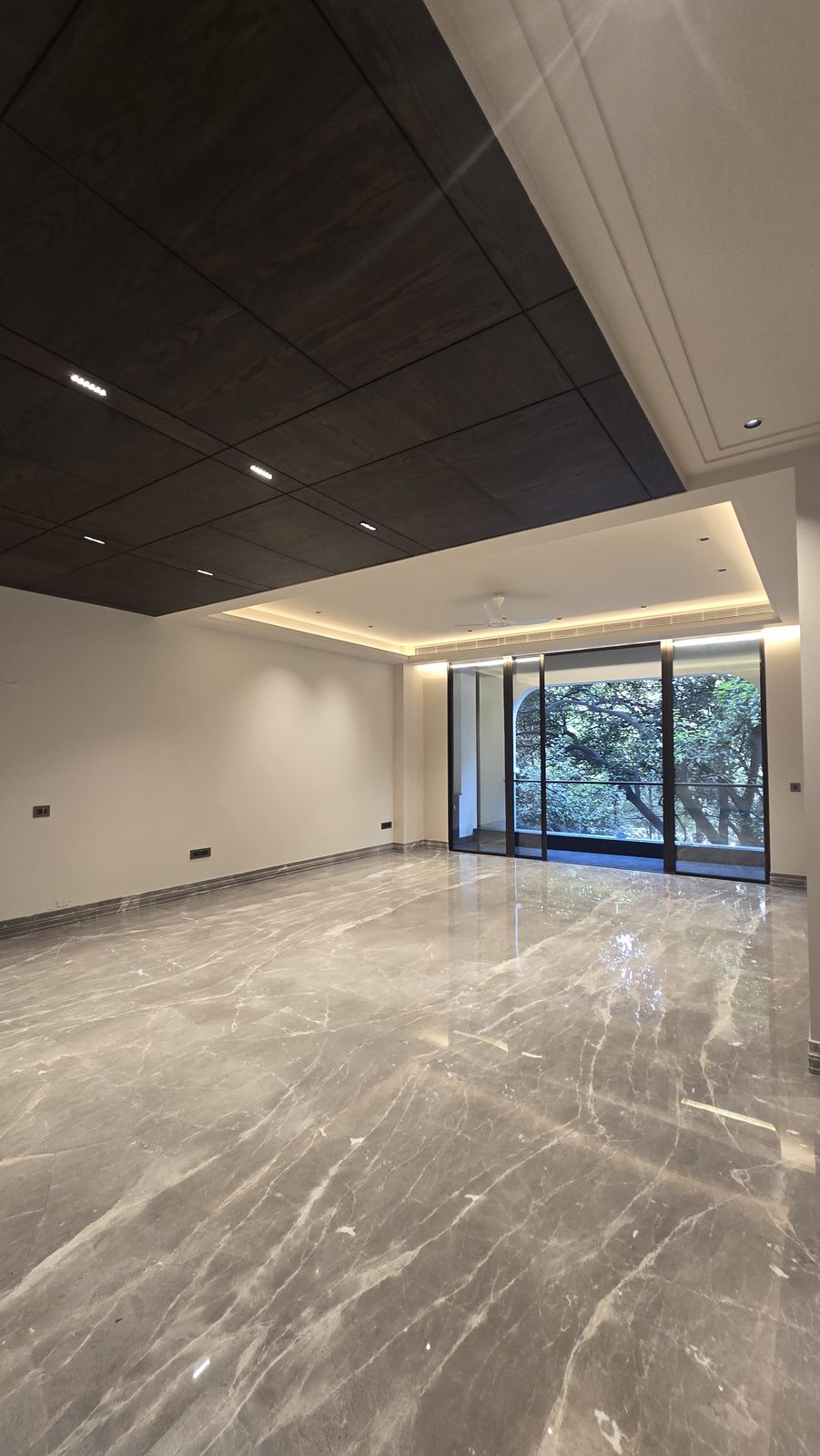 Living room with a wood-panelled ceiling and arched glazing framing mature trees in an Ekum Homes South Delhi builder floor