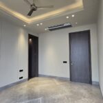 Bedroom with grey marble flooring, a cove-lit tray ceiling and a dark wood door at an Indus Homes luxury home in South Delhi