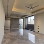 Spacious living room with glossy grey marble floor, wood-panelled feature wall and balcony doors at an Indus Homes luxury home in South Delhi