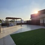 Rooftop terrace with a wooden pergola, marble bar and artificial-grass lawn at sunset at an Indus Homes luxury property in South Delhi