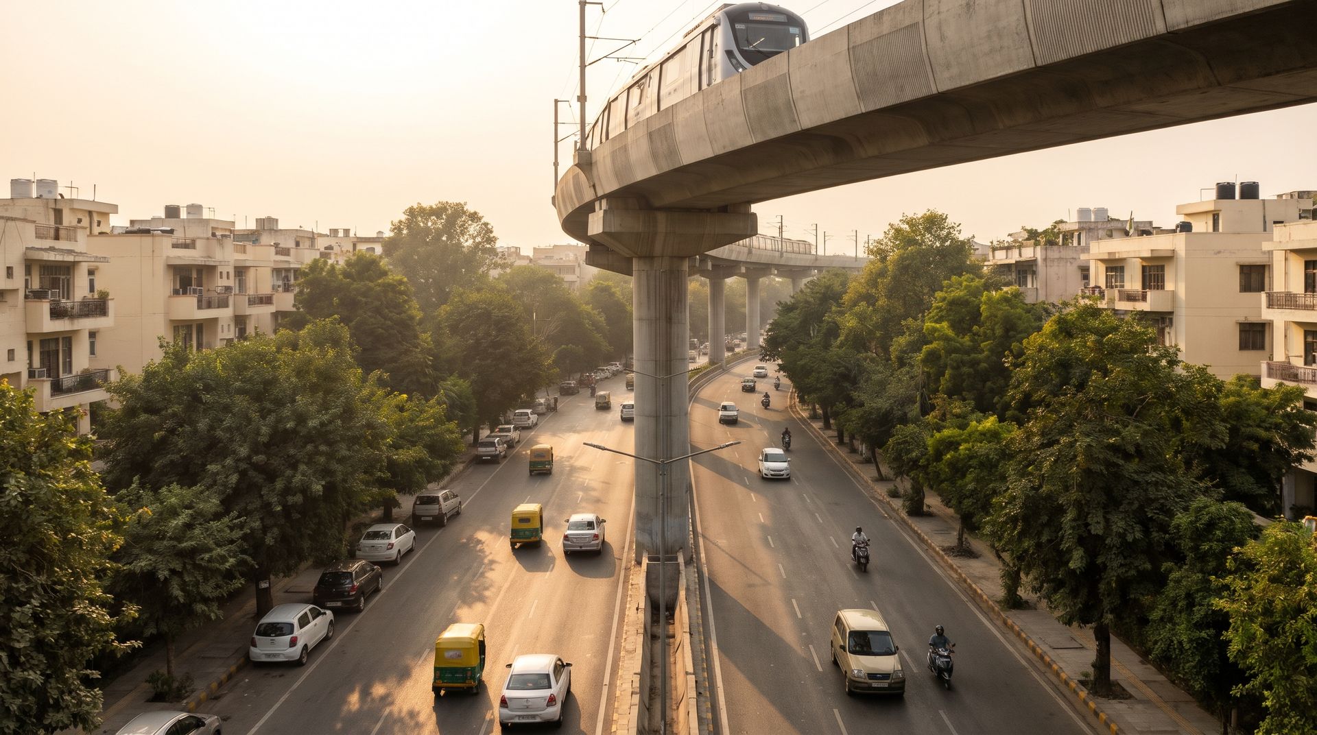 An elevated Delhi Metro viaduct curving above a tree-lined South Delhi arterial road at golden hour