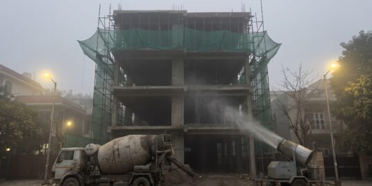 GRAP construction ban Delhi — a halted South Delhi builder floor site in winter smog with an anti-smog gun spraying