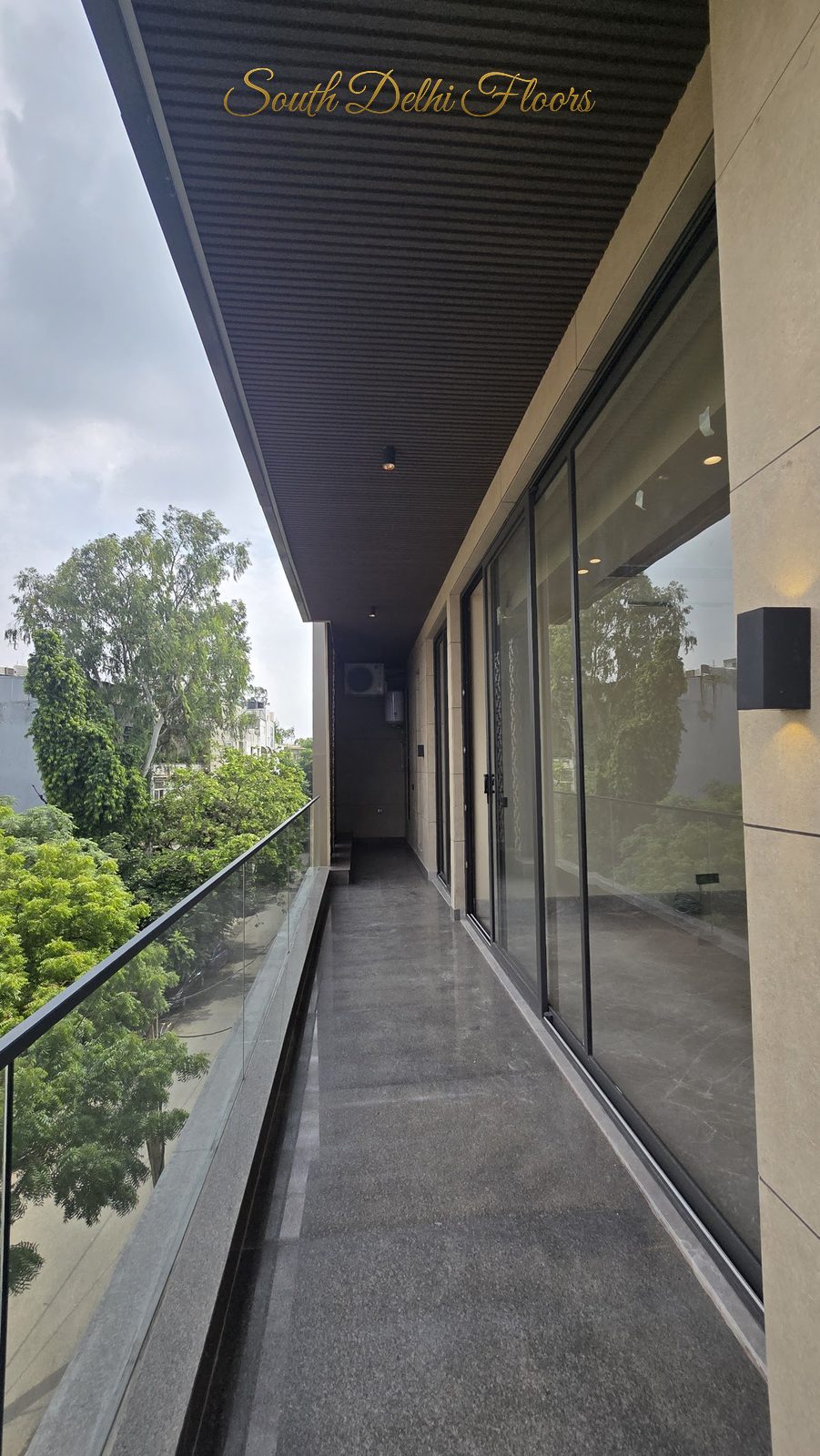 Balcony with glass railing overlooking mature trees at an Indus Homes builder floor in GK-1, South Delhi