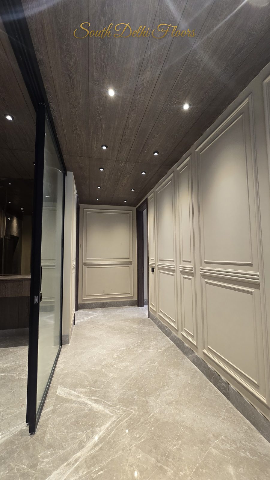Foyer passage with moulded wall panelling, fluted-glass partition and timber-clad ceiling at an Indus Homes builder floor in GK-1, South Delhi