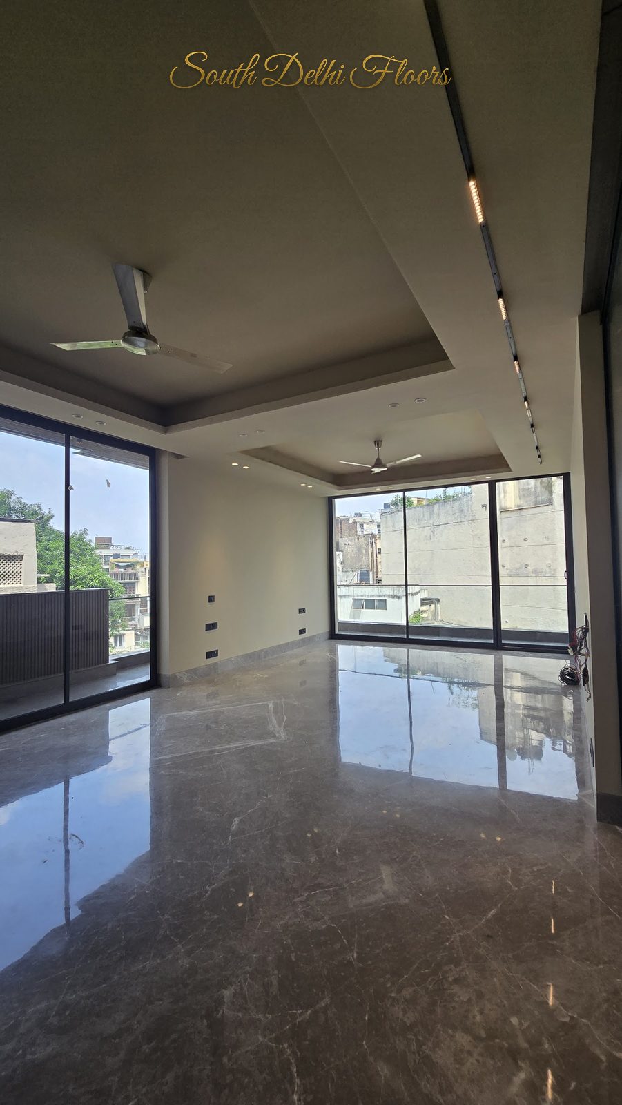 Living room with full-height sliding glazing on two sides opening to the wraparound balcony at an Indus Homes builder floor in GK-1, South Delhi
