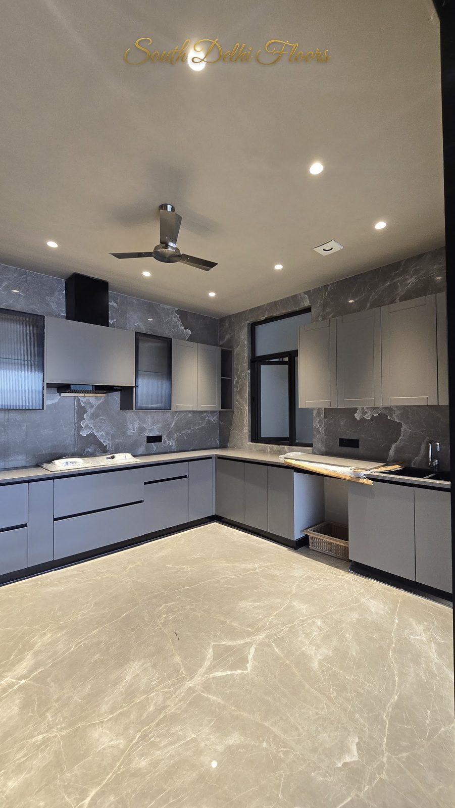 Grey modular kitchen with marble-pattern stone backsplash, built-in oven column and chimney hob at an Indus Homes builder floor in GK-1, South Delhi