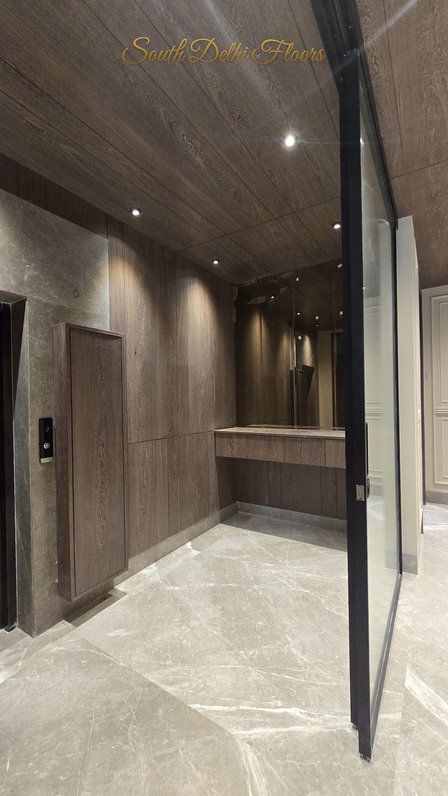 Private lift landing with wood-panelled walls and a fluted-glass security door at an Indus Homes builder floor in Greater Kailash-1, South Delhi