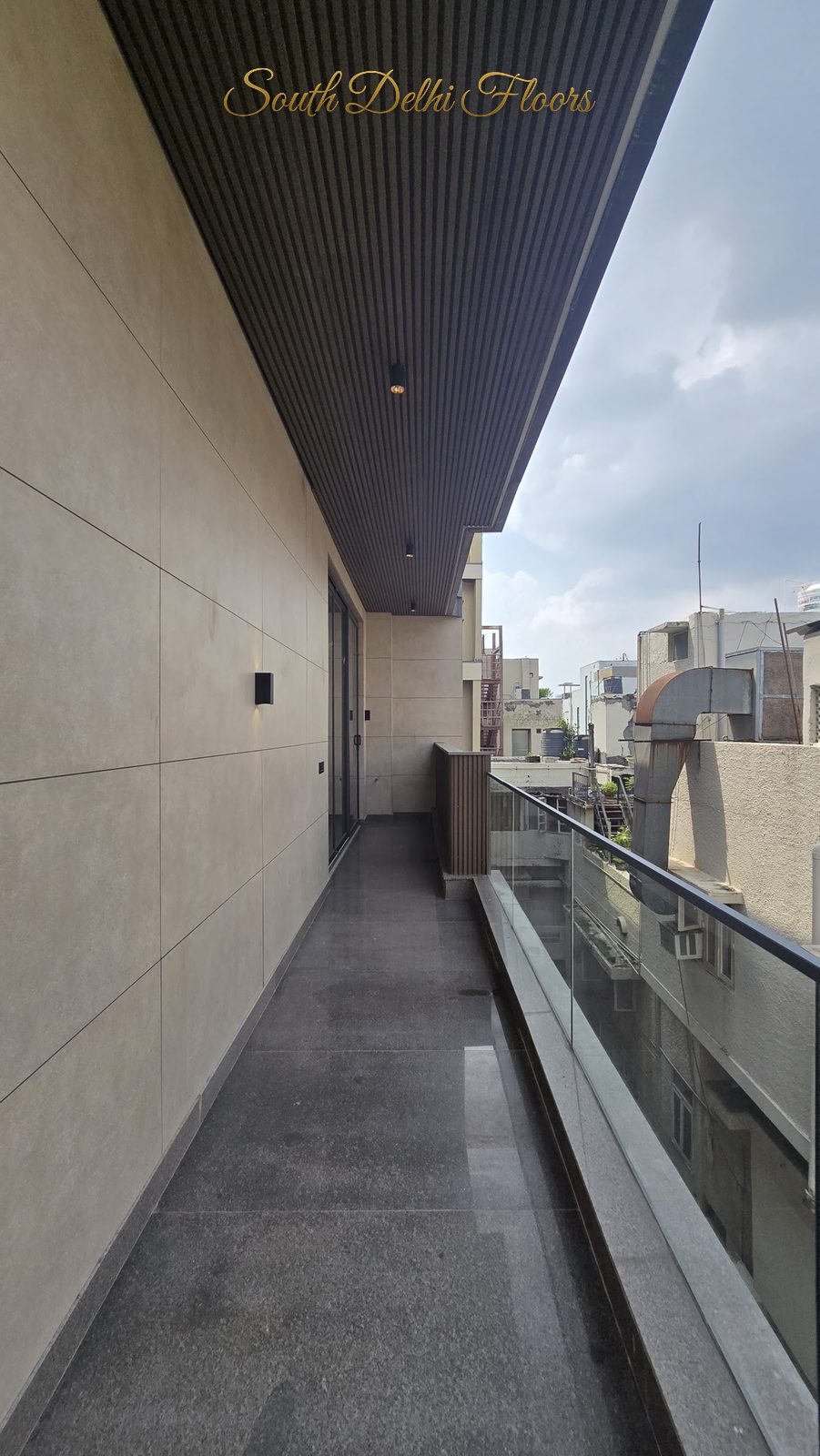 Wraparound balcony with glass railing, stone-clad wall and slatted timber ceiling at an Indus Homes builder floor in Greater Kailash-1, South Delhi