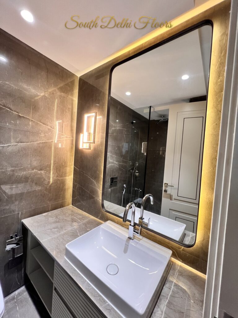 Bathroom with a warm backlit mirror, geometric LED sconce and dark veined marble walls at a Katarias luxury home in South Delhi by builder Sandeep Kataria