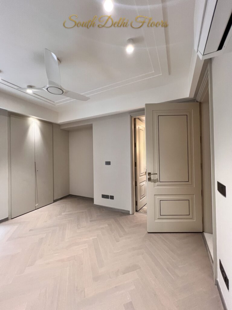 Bedroom with light herringbone flooring, a panelled door and built-in wardrobes at a Katarias luxury residence in South Delhi by developer Sandeep Kataria