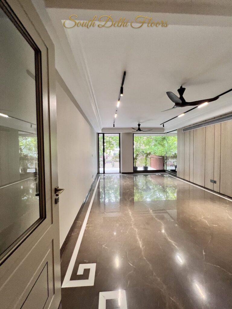 Drawing room seen through a glass-panelled door, with brown veined marble flooring and track lights at a Katarias luxury property in South Delhi by Sandeep Kataria