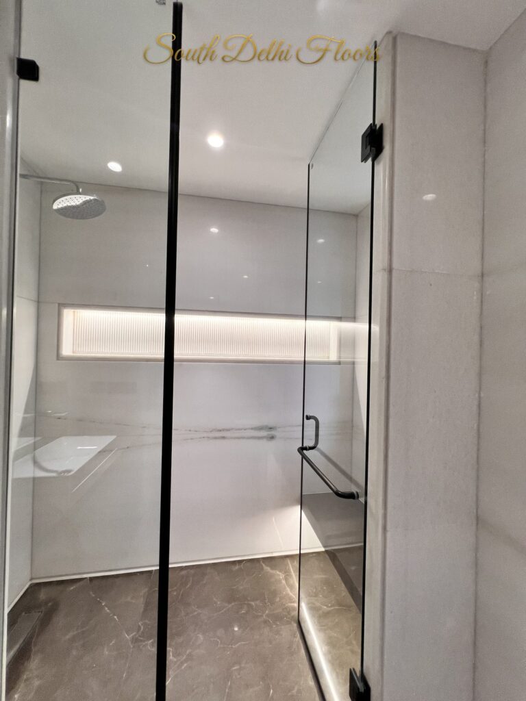 Glass shower cubicle with an overhead rain shower and white marble walls at a Katarias luxury property in South Delhi by Sandeep Kataria