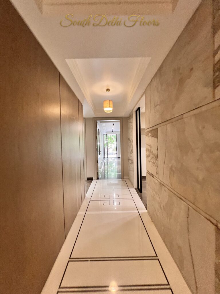Hallway with a Greek key marble floor inlay leading to a glass door and garden view at a Katarias luxury builder floor in South Delhi by Sandeep Kataria