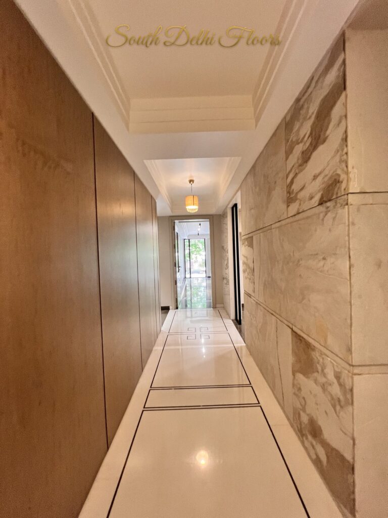 Hallway pairing wood wall panels with large veined marble slab cladding and a cove ceiling at a Katarias luxury residence in South Delhi by developer Sandeep Kataria