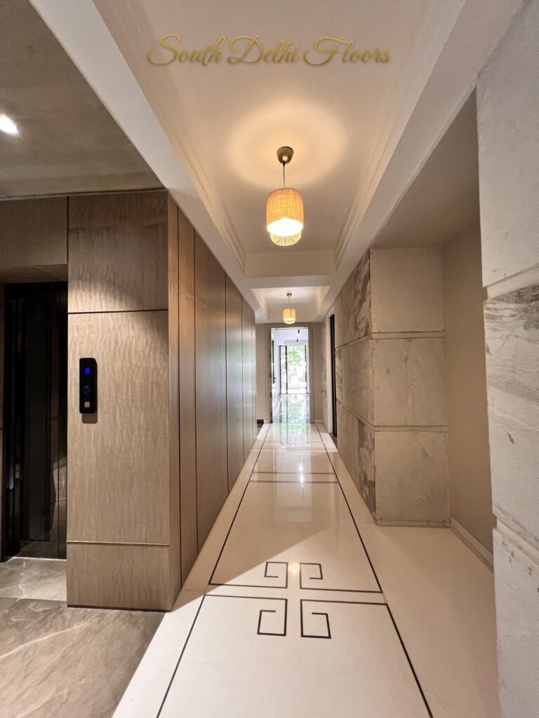 Lift landing opening onto a marble corridor with a Greek key inlay and stone-clad walls at a Katarias luxury home in South Delhi by builder Sandeep Kataria
