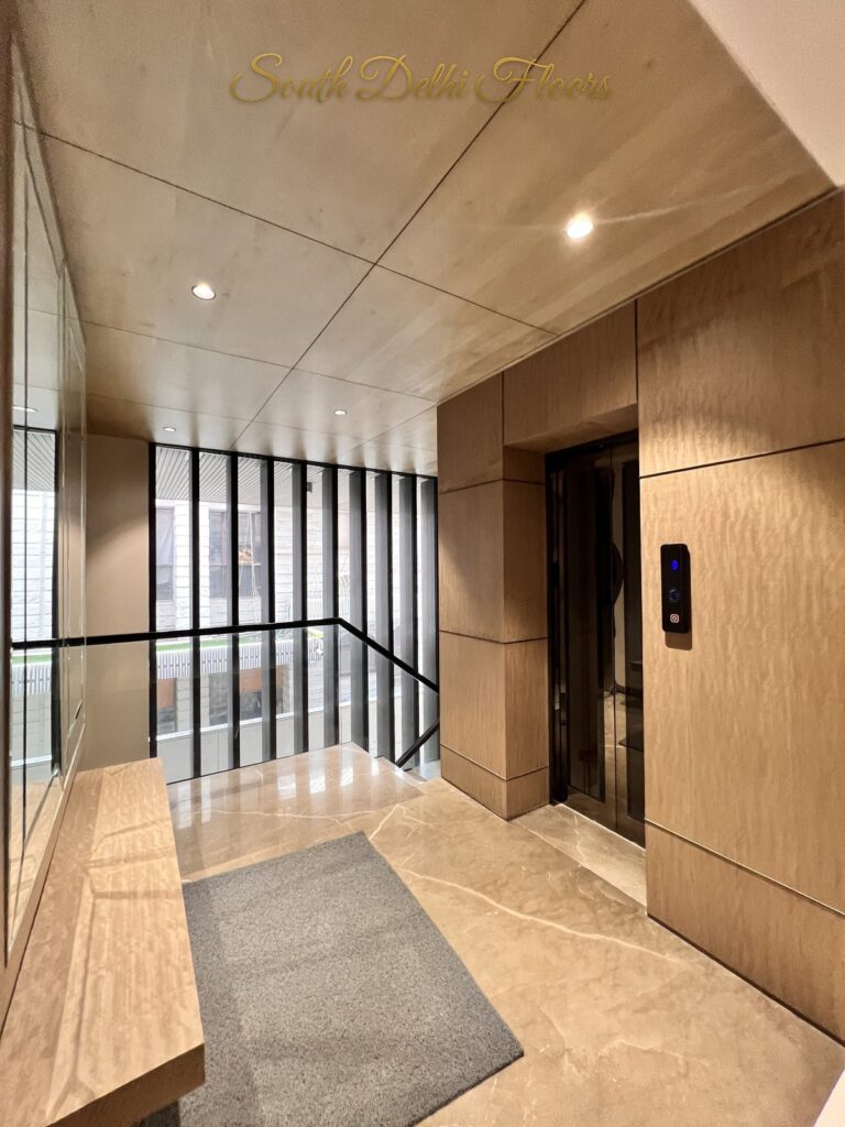 Lift lobby with a wood veneer lift portal, wooden bench and louvred glazing onto the stairwell at a Katarias luxury builder floor in South Delhi by Sandeep Kataria