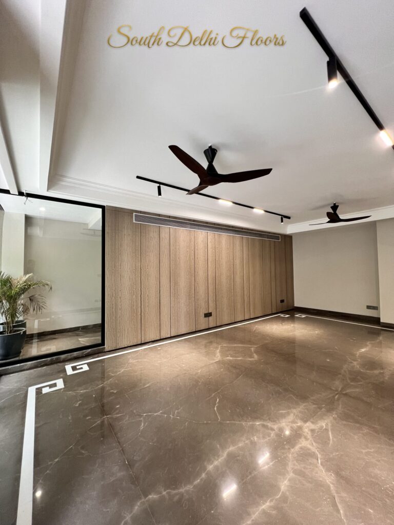Living room with a black-framed glass partition, an indoor palm and brown marble flooring at a Katarias luxury builder floor in South Delhi by Sandeep Kataria