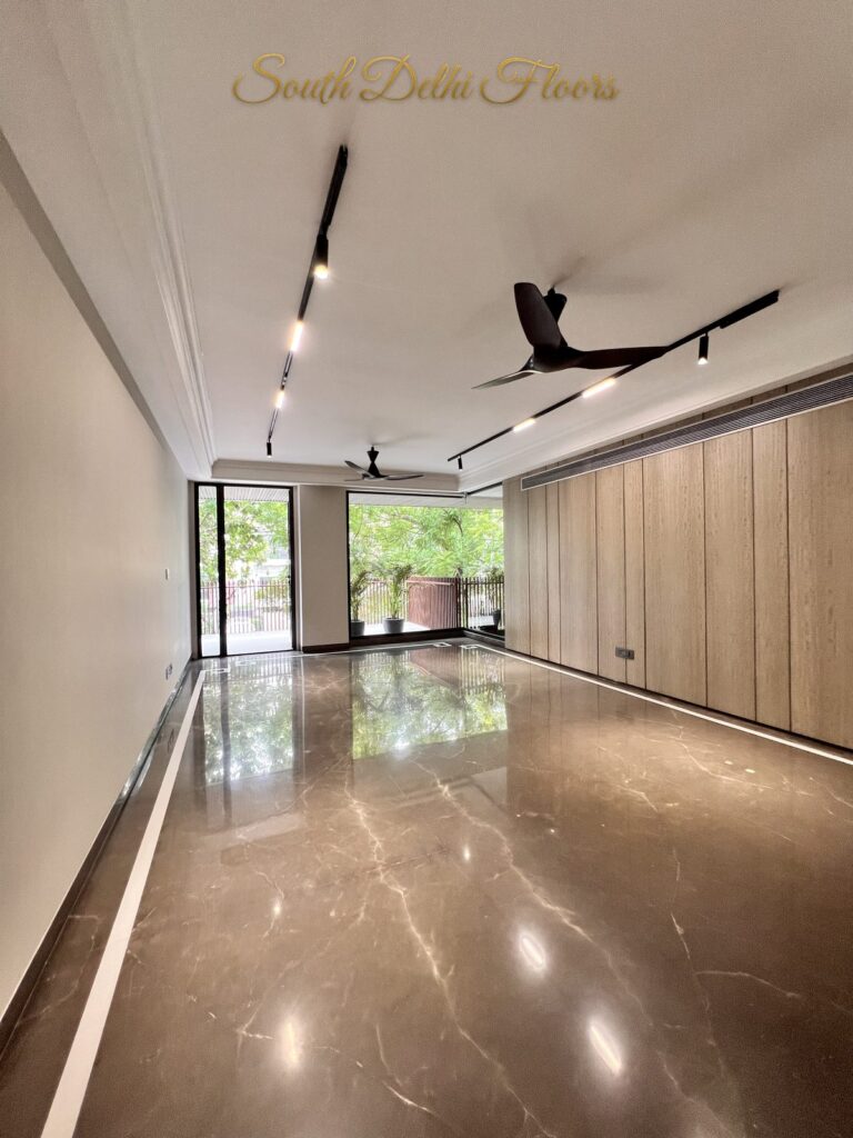 Living room with a wood-panelled wall and full-height windows looking onto greenery at a Katarias luxury residence in South Delhi by developer Sandeep Kataria