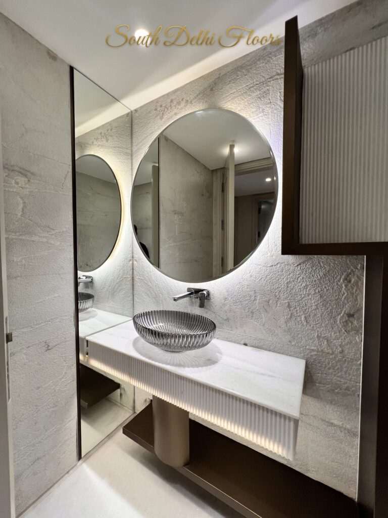 Ribbed glass vessel basin on a fluted white vanity beneath a round backlit mirror at a Katarias luxury property in South Delhi by Sandeep Kataria