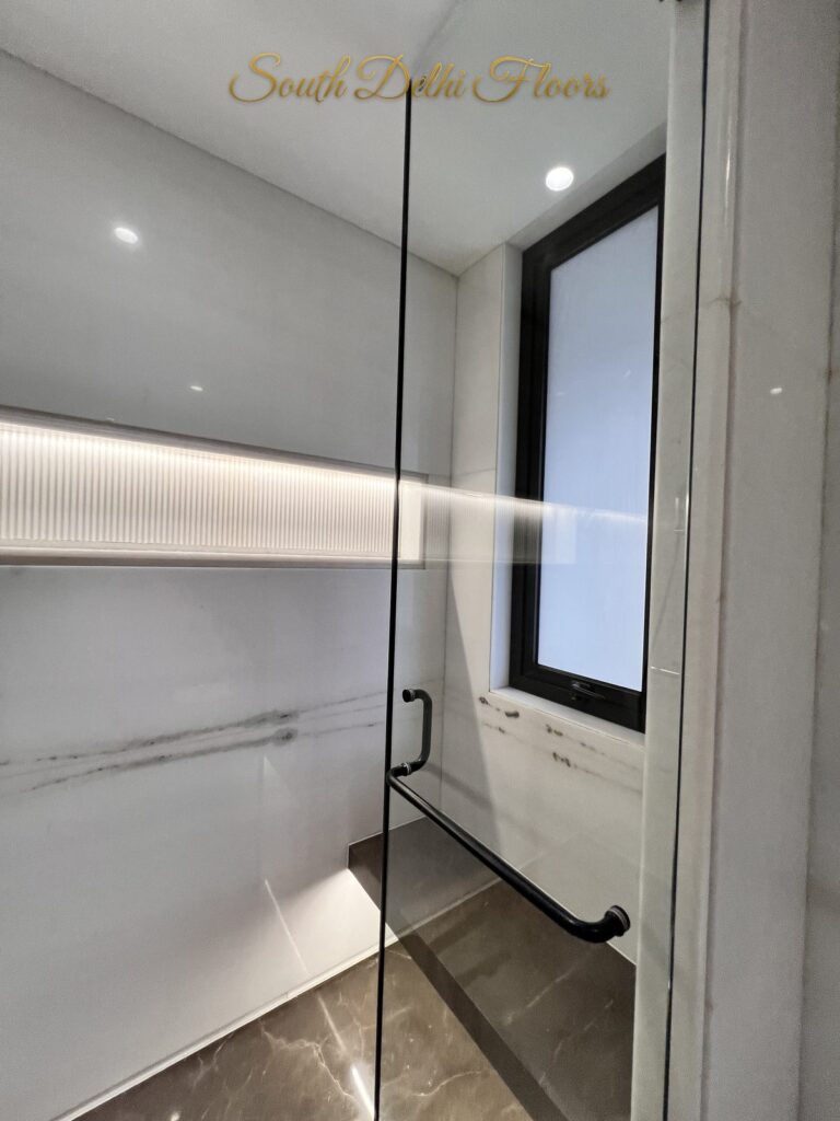 Shower with an illuminated fluted niche, black towel bar and a window at a Katarias luxury builder floor in South Delhi by Sandeep Kataria