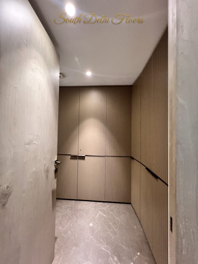 Walk-in wardrobe with fluted wood veneer shutters, integrated handles and grey marble flooring at a Katarias luxury builder floor in South Delhi by Sandeep Kataria