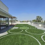 Rooftop terrace garden with a patterned lawn and glass-walled lounge in a home by the developer of the penthouse in Pamposh Enclave