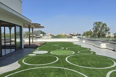 Rooftop terrace garden with a patterned lawn and glass-walled lounge in a home by the developer of the penthouse in Pamposh Enclave