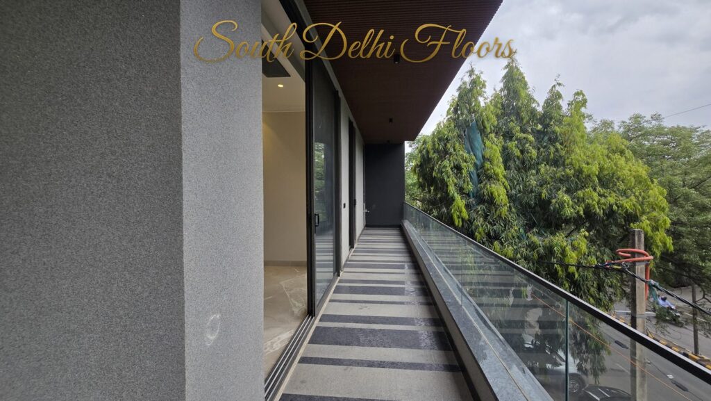 Balcony with glass railing, striped floor and green canopy view at an RPB Homes JCR Homes luxury property in South Delhi by Mahavir Bihani and Rajat Bihani