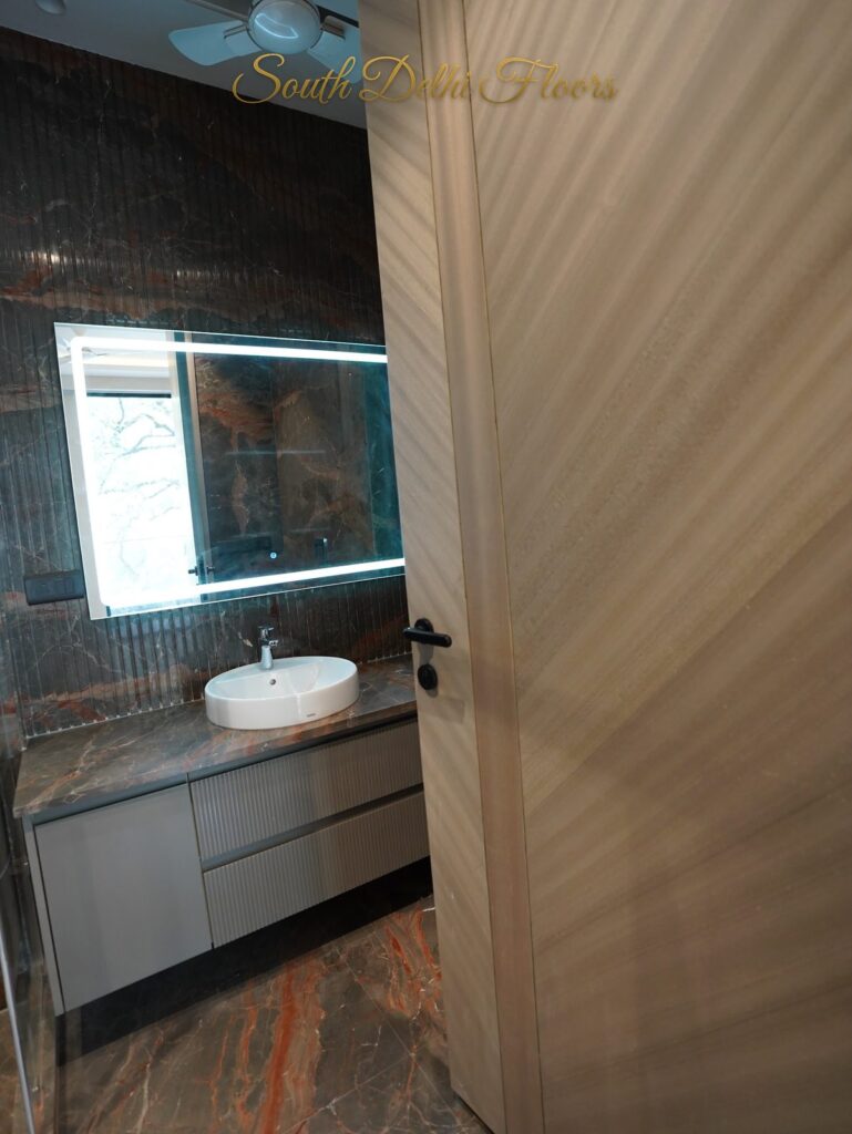 Bathroom with rust-veined marble walls, a backlit mirror and floating vanity at an RPB Homes JCR Homes luxury builder floor in South Delhi by Mahavir Bihani and Rajat Bihani