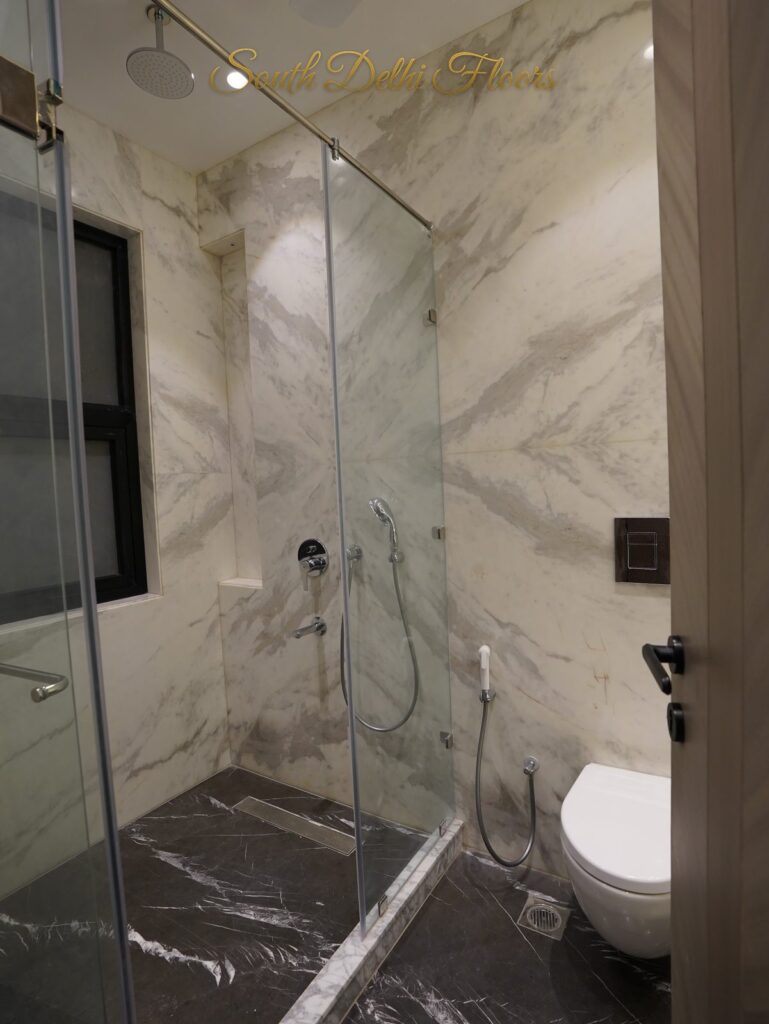 Bathroom with white marble walls, a glass shower cubicle and wall-hung WC at an RPB Homes JCR Homes luxury builder floor in South Delhi by Mahavir Bihani and Rajat Bihani