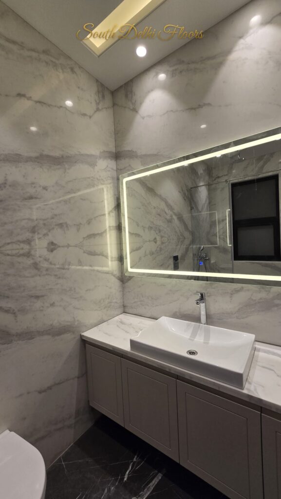 Bathroom with white marble walls, an LED mirror and grey shaker-style vanity at an RPB Homes JCR Homes luxury builder floor in South Delhi by Mahavir Bihani and Rajat Bihani