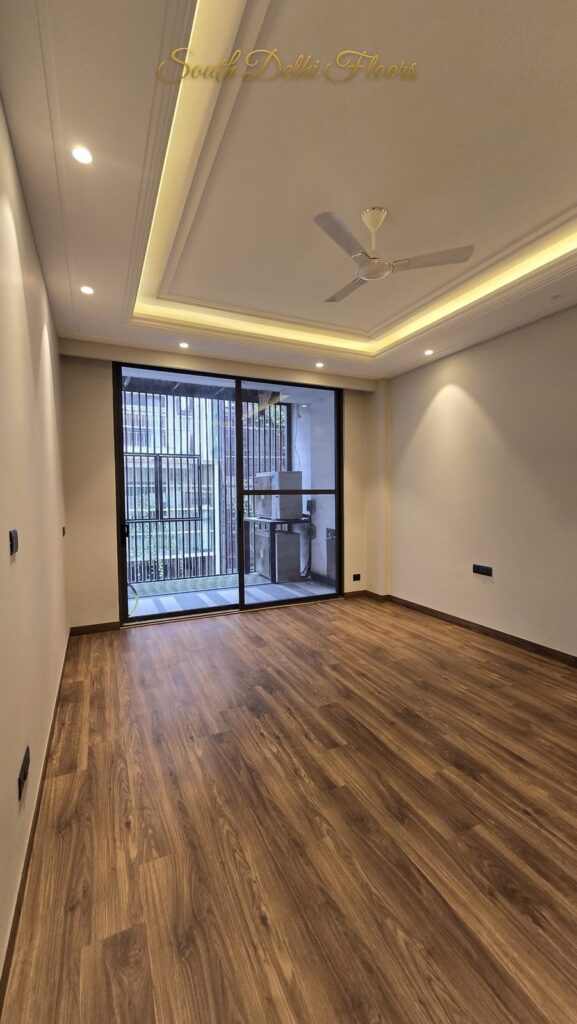 Bedroom with wooden flooring, a cove ceiling and balcony glass door at an RPB Homes JCR Homes luxury home in South Delhi by builders Mahavir Bihani and Rajat Bihani