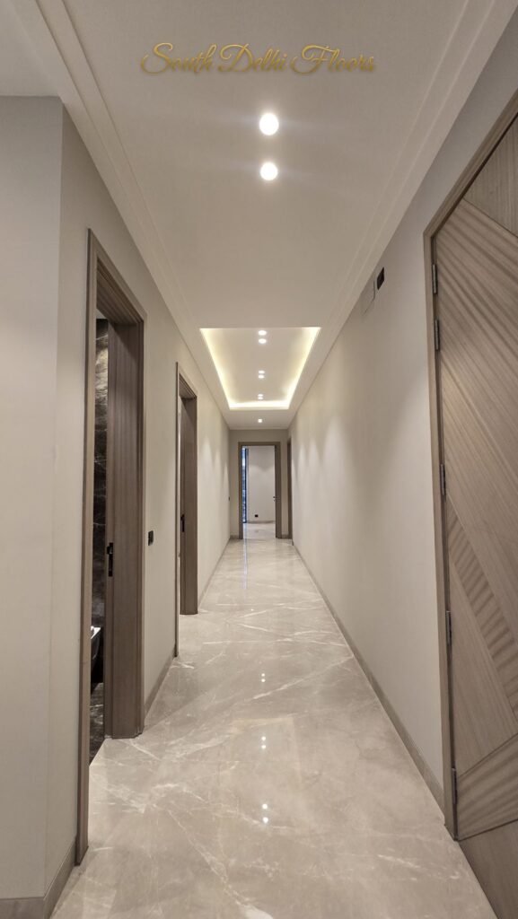 Corridor with chevron wooden doors, cream marble floor and cove lighting at an RPB Homes JCR Homes luxury builder floor in South Delhi by Mahavir Bihani and Rajat Bihani