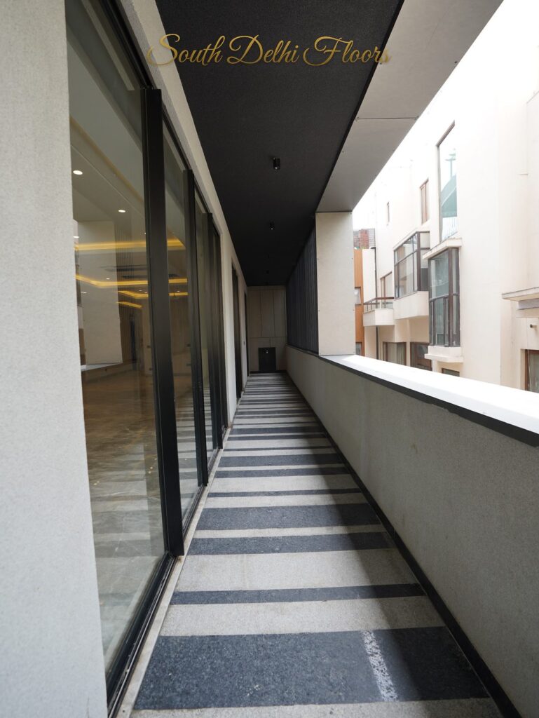 Long balcony with striped granite flooring and black-framed glass sliding doors at an RPB Homes JCR Homes luxury home in South Delhi by builders Mahavir Bihani and Rajat Bihani