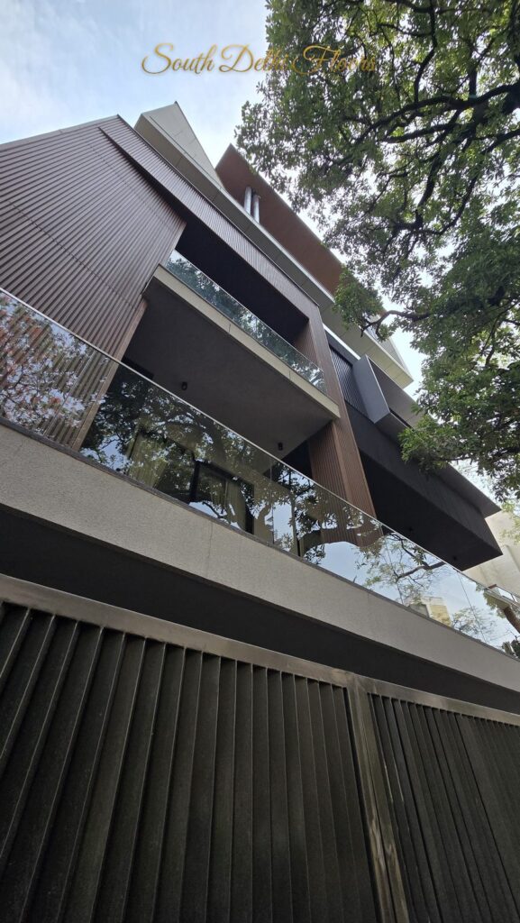 Modern facade with wooden louvers, glass balconies and mature trees at an RPB Homes JCR Homes luxury builder floor in South Delhi by Mahavir Bihani and Rajat Bihani