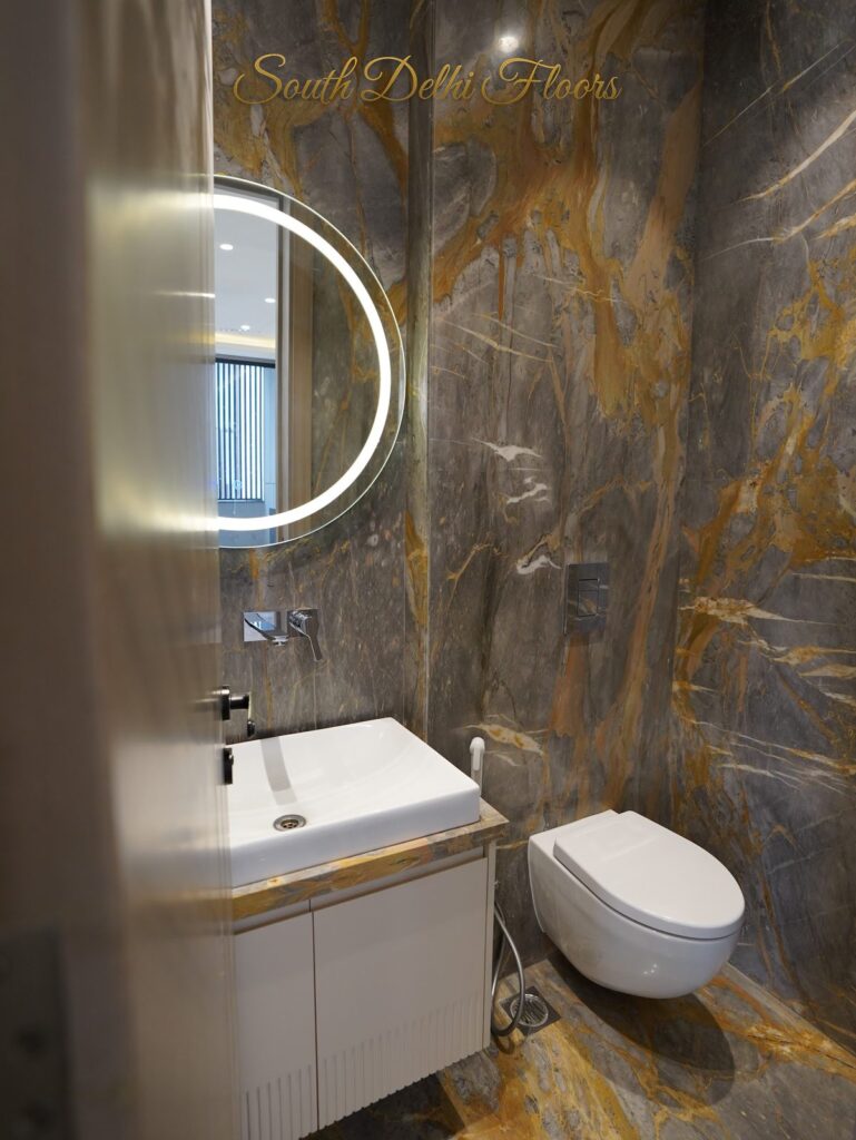 Powder room with gold-veined marble, a half-moon LED mirror and wall-hung WC at an RPB Homes JCR Homes luxury home in South Delhi by builders Mahavir Bihani and Rajat Bihani