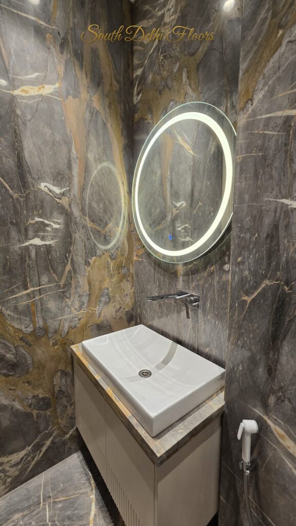 Powder room with grey and gold veined marble, a round LED mirror and countertop basin at an RPB Homes JCR Homes luxury builder floor in South Delhi by Mahavir Bihani and Rajat Bihani