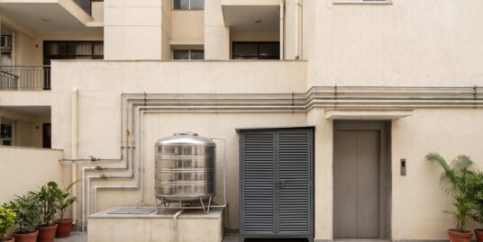 The service area of a South Delhi builder floor building showing water pipes, an overhead tank, a generator and the lift machine room